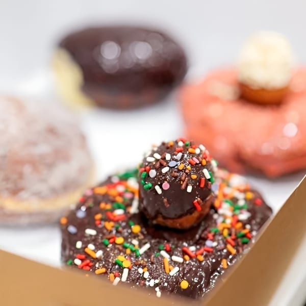 A box of assorted Dough Miner donuts, including chocolate with sprinkles and powdered sugar.