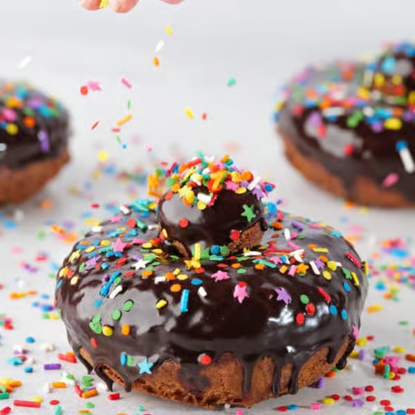 Chocolate-glazed donuts from The Dough Miner, topped with colorful sprinkles, with more sprinkles falling.