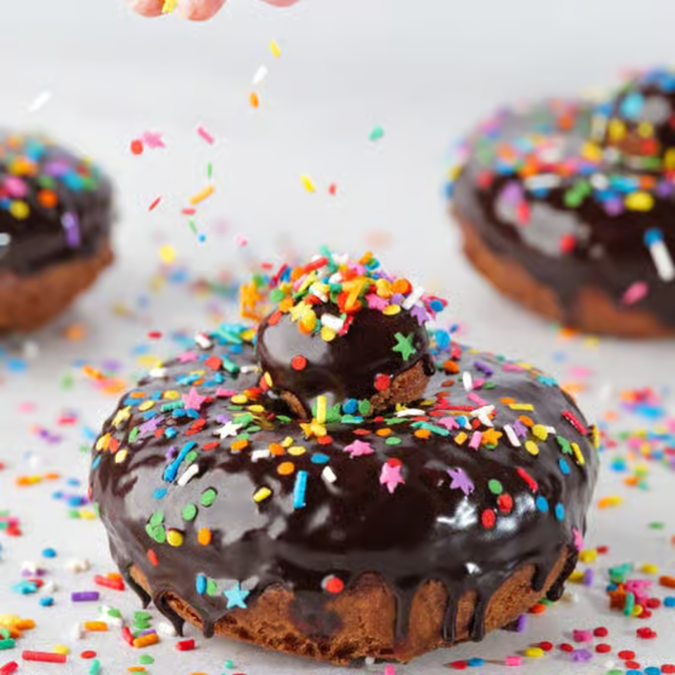 Chocolate-glazed donuts from The Dough Miner, topped with colorful sprinkles, with more sprinkles falling.