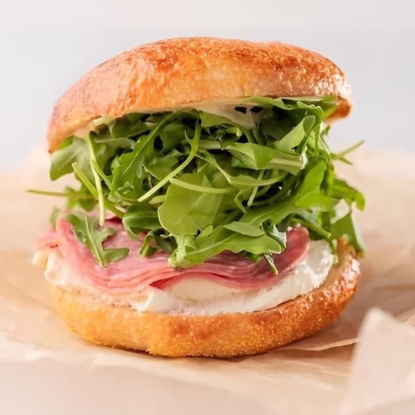 A Dough Miner sandwich with salami, cheese, and arugula on a toasted bun.