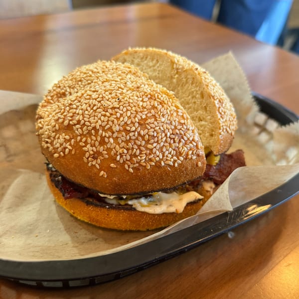 A sesame seed bun sandwich with meat and sauce, served in a basket on a wooden table.