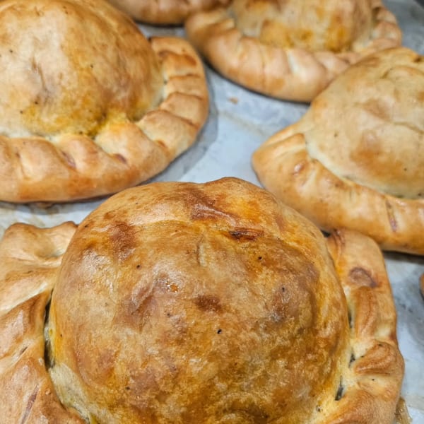 Several golden-brown, freshly baked pasties with crimped edges from The Dough Miner bakery.