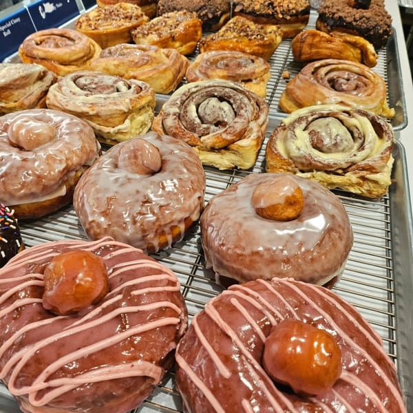 A tray filled with various glazed donuts and cinnamon rolls from The Dough Miner bakery.